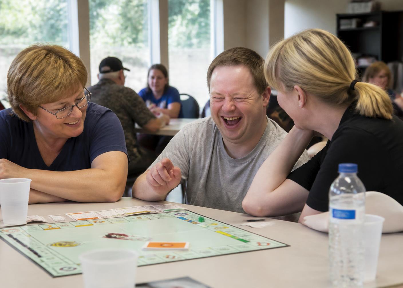 An adult man and two friends laughing over a board game at a community center table